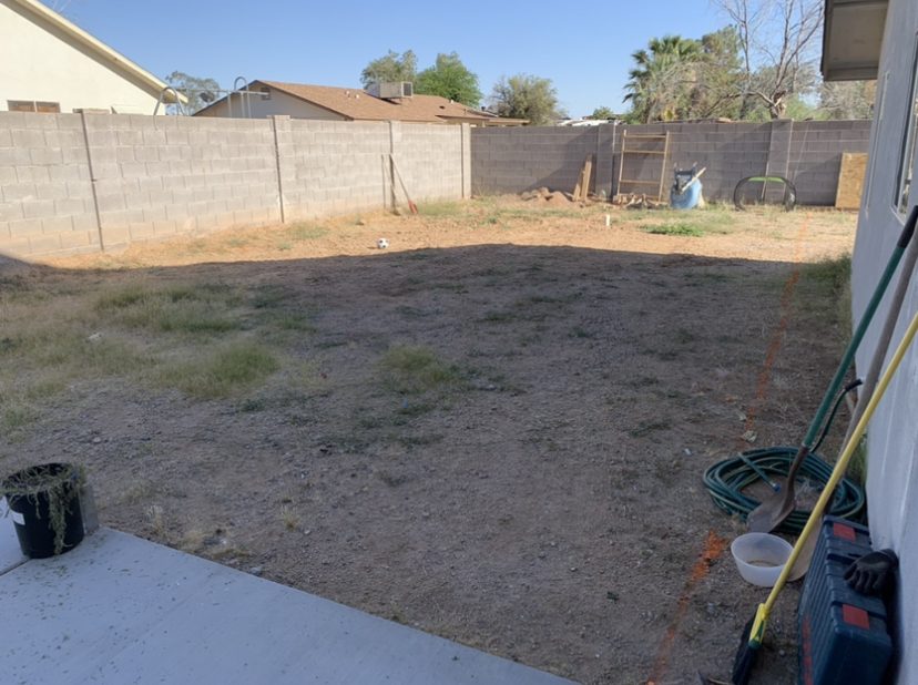 before image of a blank dirt yard with weeds and a block wall