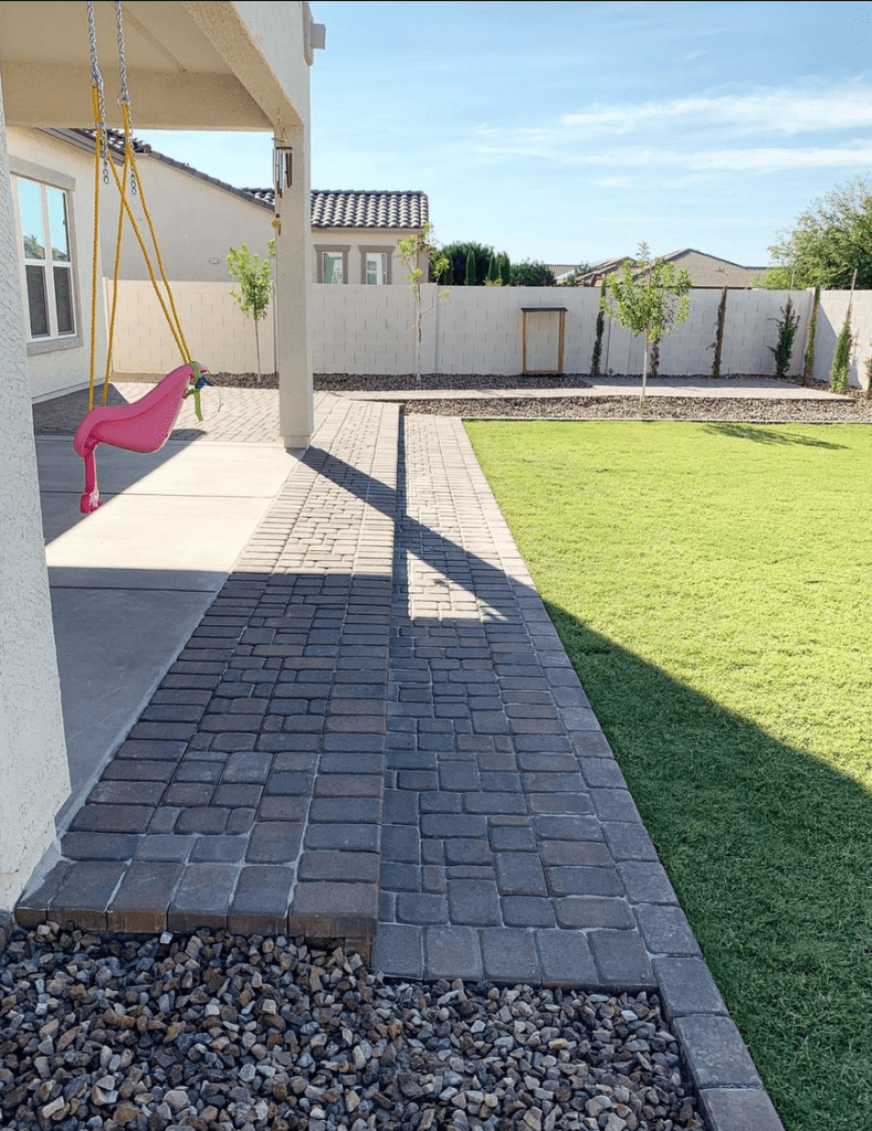 two sets of paver steps from a patio into an artificial turf lawn.