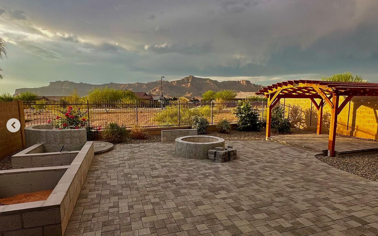 after view of a pergola and paver filled backyard with planters and a fire pit